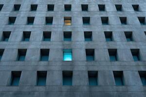 gris hormigón edificio fachada con uno iluminado ventana en el noche foto