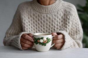 Cozy person holding a warm cup of tea in a knitted sweater at home photo