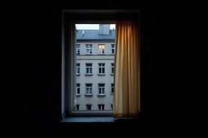 Late evening view through a window with a lit apartment in the distance photo