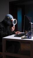 vertical hacker vestindo Pombo mascarar analisando computador ampliação vidro. espião golubiro video