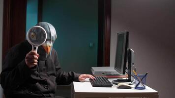 mascarado hacker usando ampliação vidro enquanto trabalhando em computador. espião golubiro video