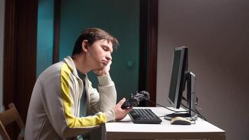 entediado jogador sentado às escrivaninha segurando controlador olhando às computador video