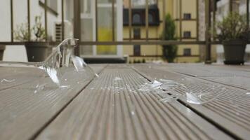 Shattering wine glass hitting wooden floor in slow motion, A wine glass breaks on impact with a wooden deck surface, captured at the moment of shattering video
