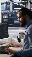 Vertical Overworked technician in data center managing server infrastructure for AI inference tasks. Fatigued employee using PC to maintain supercomputers running artificial intelligence tech, camera A video