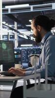 Vertical Engineer in server room responding to sudden ransomware detection on monitor, requesting help from manager to protect critical data. Worker reviewing suspicious activity logs, informing team leader, camera A video