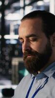 Vertical Smiling data center technician using PC to monitor neural network AI LLM visualization. Server room worker using computer to oversee rigs powering machine learning processes, camera A video