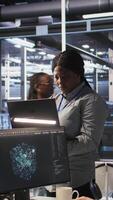 Vertical Portrait of happy technician next to data center colleagues review AI diagnostics. Cheerful IT specialist and coworkers analyze neural network performance to maintain operational reliability, camera A video
