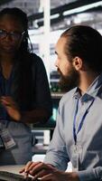 Vertical Teamworking system administrators in data center integrating AI automation during maintenance session. Server farm coworkers configuring machine learning models across equipment rigs, camera A video