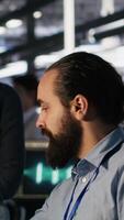 Vertical Data center system administrators working together, collaborating on neural network software development. Server hub worker and african american colleague implementing AI tech in workplace, camera A video