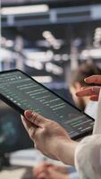 Vertical Close up of data center system administrator coding on tablet, doing software updates. Server room IT expert looking at device screen, optimizing infrastructure rackmounts configuration rigs, camera A video