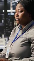 Vertical Data center programmer coding on PC, doing software updates for AI visualization systems. African american woman in server room optimizing infrastructure using artificial intelligence, camera A video