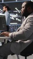 Vertical Exhausted server farm employee stretching back after sitting too long at computer desk. Fatigued man in data center office relaxing muscles, stressed by long hardware troubleshooting session, camera A video