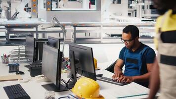 African american engineer manages data from solar machinery on desktop, working in a solar panel manufacturing factory. Male technician in automated renewable energy production line. Camera B. video