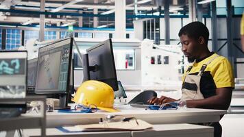 Black worker programming robotic assembly line in solar cell factory, working with high tech software for automation. Male engineer testing photovoltaic system, machinery. Camera B. video