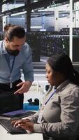 Vertical Server room manager providing feedback to employee managing AI training datasets. Team leader talking with technician in data center supervising system operations supporting neural networks, camera A video