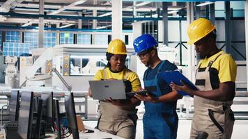Group of black employees at the solar panels factory reviewing data on devices and documents. Photovoltaics facility engineers working on innovative solar cells design prototype. Camera B. video