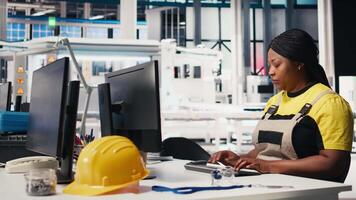 Technician monitors manufacturing data on pc in solar panel factory, employee finetunes equipment settings to support efficient solar power production. Woman seated next to assembly line. Camera A. video