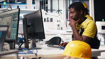 Male specialist adjusts machine parameters for solar panel production, working at a high tech manufacturing plant. Black engineer analyzing technical data on a computer. Camera B. video