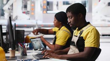 Black employee manages solar panel configuration via desktop tools, optimizing factory output and troubleshooting. Technician updates energy system parameters on pc. Camera A. video
