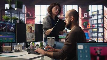 In professional production office, team discusses content strategy and trends while reviewing footage on computers, aiming to increase followers and viral potential across platforms. Camera A. video