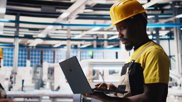 Male engineer in solar panel factory reviews photovoltaic system performance on laptop. Specialist analyzing production line on notebook to optimize efficiency, troubleshooting. Camera B. video