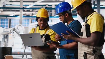 Technicians group in photovoltaics factory use tracking software on devices, troubleshooting for seamless production line. Black team reviews robot arms manufacturing solar panels. Camera A. video