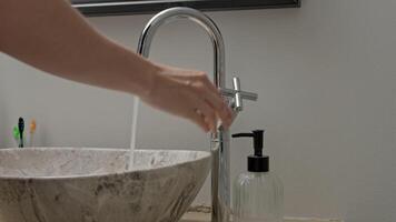 Hand turns on faucet as water flows into bathroom sink. video