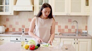 Woman in bright kitchen slicing cucumber and singing while making a fresh salad video