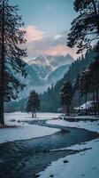 A river flows through a snowy field with trees and mountains in the background photo