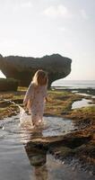 Little child girl playing in a puddle on ocean shoreline. Happy childhood with sunset sunshine video