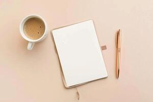 A cup of coffee sits on a table next to a pen and a blank notebook photo