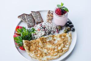 Delicious breakfast plate featuring an omelet, fresh vegetables, and yogurt dessert with berries. photo