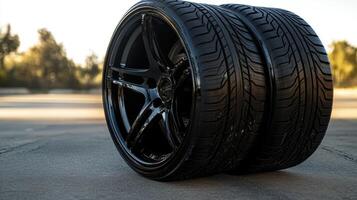 Two shiny black car tires with stylish rims on outdoor concrete surface reflecting sunlight in an automobile maintenance setting. Tires with rubber tread on alloy wheels photo