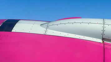 Close-up view of pink and white airplane fuselage against clear blue sky highlighting modern aviation design aesthetics and engineering precision photo