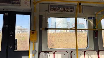 Interior view of modern city tram showing window reflections and urban landscape in daylight with yellow handrails and ticket validator photo