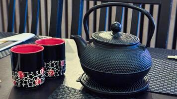 Elegant black cast iron tea kettle with red and black patterned mugs on dining table in cozy indoor setting enjoying warm beverage photo