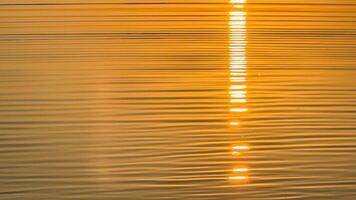 Golden sunset reflection on rippling water creating a warm tranquil ambiance with striking horizontal light patterns on the surface photo