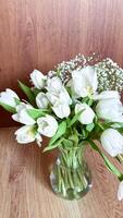 Elegant bouquet of white tulips in glass vase with baby's breath on wooden surface capturing the essence of minimalist floral decor photo