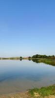 Serene lakeside landscape with clear blue sky and verdant greenery reflecting tranquility and natural beauty in a peaceful, scenic view photo