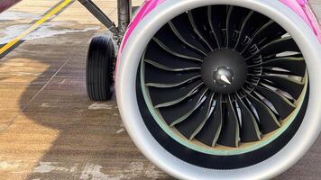 Close-up view of a large modern jet engine with distinctive pink and silver colors on a concrete runway photo