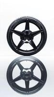 Sleek black car tire reflecting symmetry on glossy surface showcases modern automotive design and engineering precision. Tires with rubber tread on alloy wheels photo
