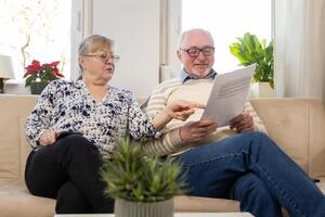 couple of elderly migrants sit on sofa with papers in their hands. They read letters from government agenciestry to translate the text. Not knowing the language makes it difficult for them to adapt photo