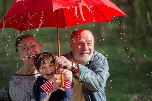 Grandfather and grandson are holding an umbrella, and grandmother is looking at them. The scene is fun and light-hearted. family in the rain. photo