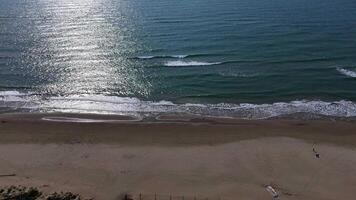 Serene beach view at midday with gentle waves lapping at the shore and sunlight glistening on the water video