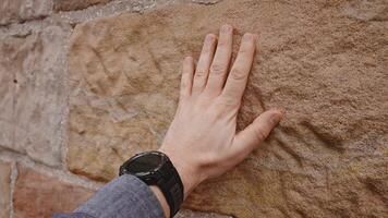 A close-up of a man's hand touching a textured stone wall. The hand is positioned flat against the rough surface, showcasing the contrast between human skin and natural rock. video