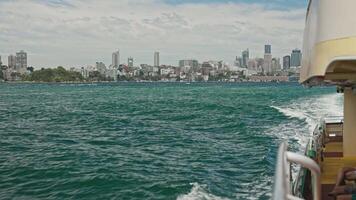 A shot from aboard a Sydney ferry crossing the harbor captures distant parklands and the city center, with churning wake trailing behind the vessel. video