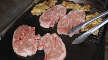 Fresh pork chops and marinated chicken pieces are sizzling on a hot grill. The raw pork is still pink with visible marbling, while the chicken has a golden-brown, slightly charred surface. video
