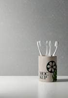 Three toothbrushes stand upright in a cylindrical holder adorned with a floral design and the word MOCKUP psd