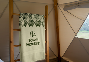 A neatly folded towel with a nature inspired design hangs on a wooden ladder inside a glamping tent psd