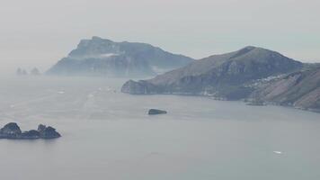 A serene aerial view of the Amalfi coastline in Italy, showcasing rugged cliffs, rocky islets, and a misty sea with gradual panning motion. video